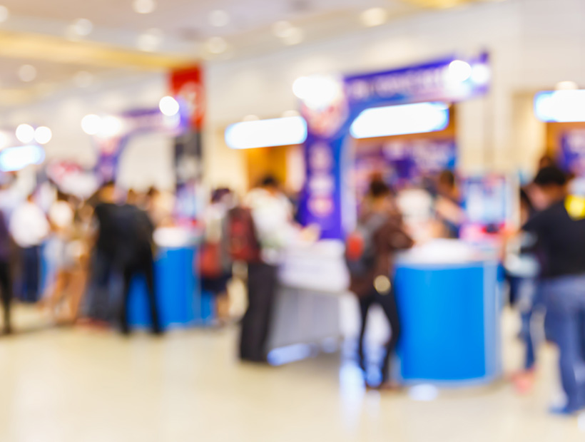 Blurred image depicting a crowd of people navigating through a bustling shopping mall environment.